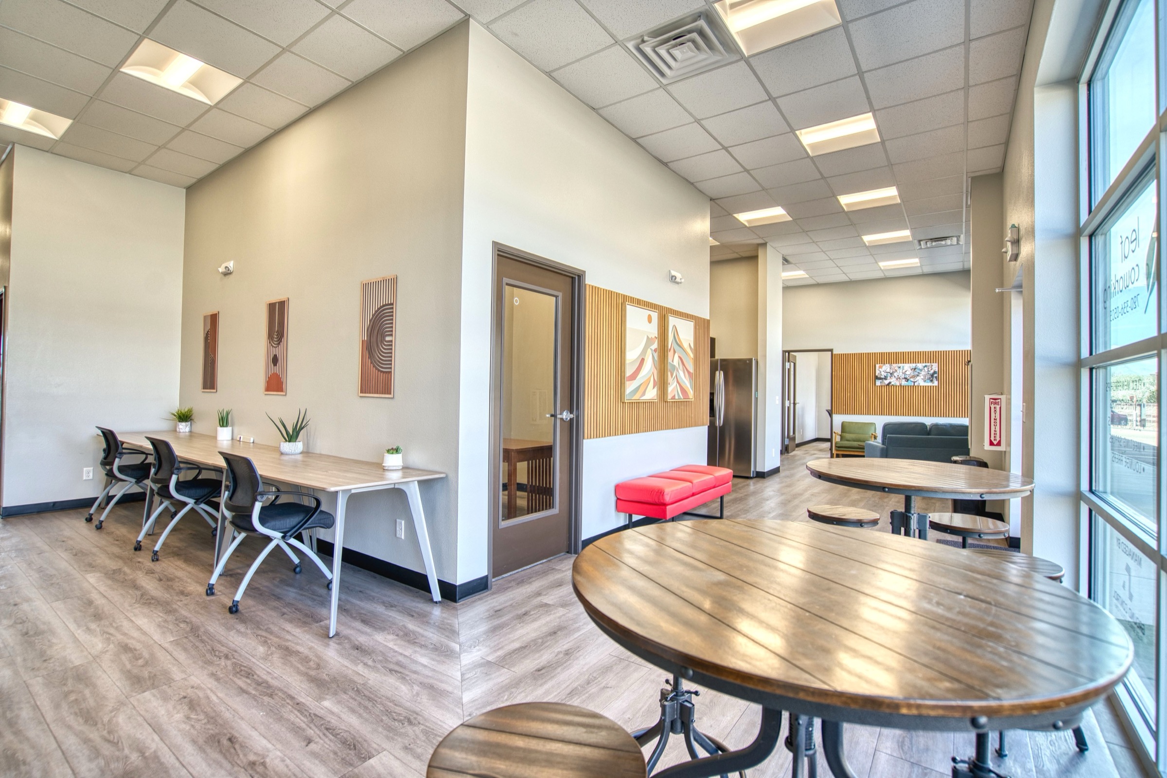 Open coworking area with shared work desks, rolling chairs, round bistro tables, and view into the lobby lounge