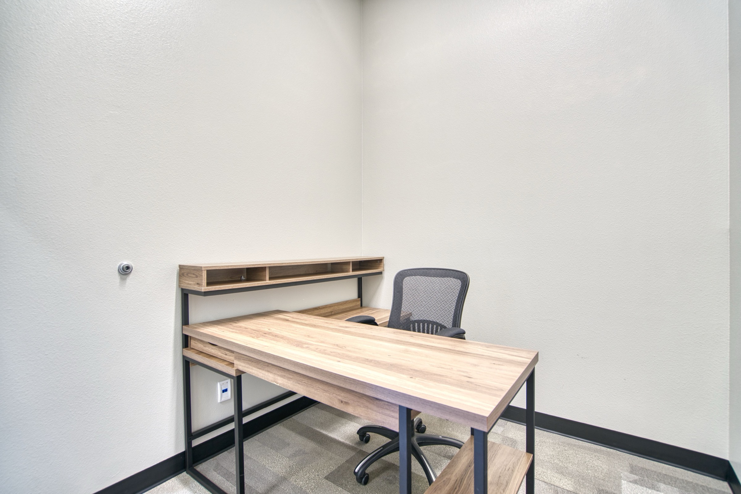 Dedicated desk workspace with butcher-block wood desk, metal frame, ergonomic mesh chair, and wall-mounted shelf