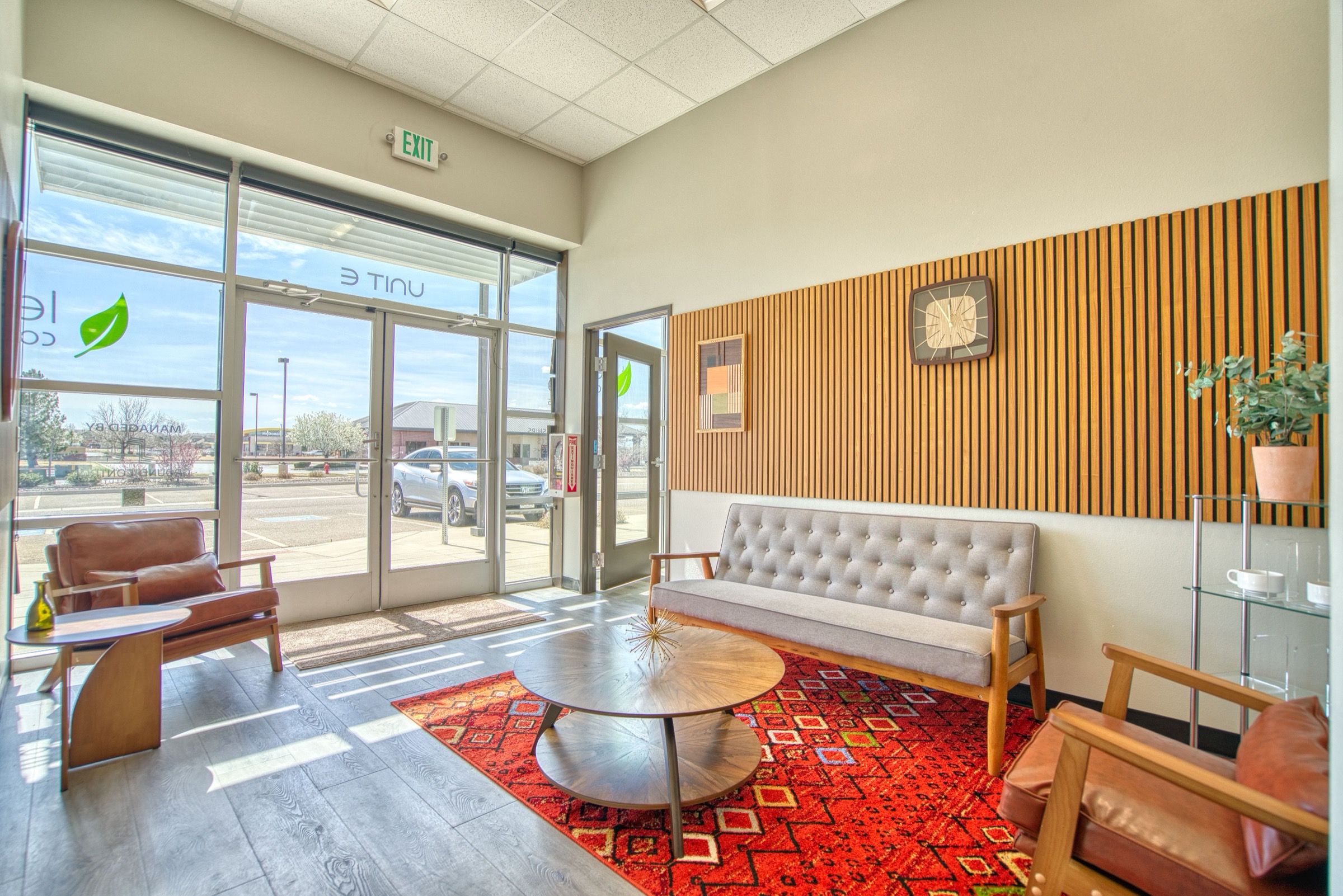 Leaf Coworking entry lobby with natural light streaming through glass front doors, Leaf logo visible, and mid-century lounge furniture
