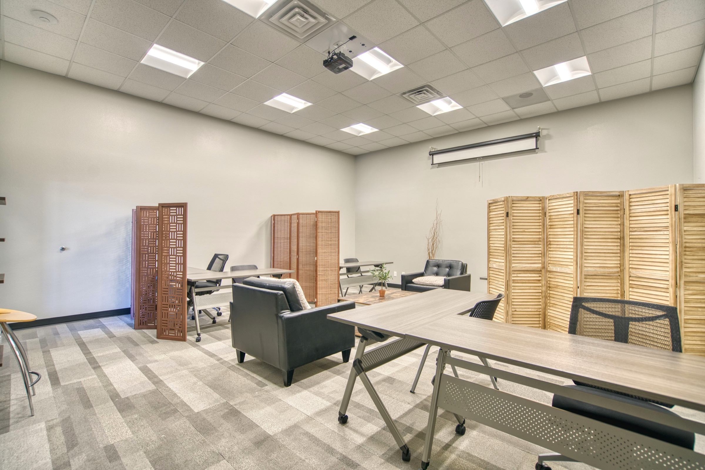 Large flexible event space with ceiling-mounted projector, folding tables, and decorative wood room dividers