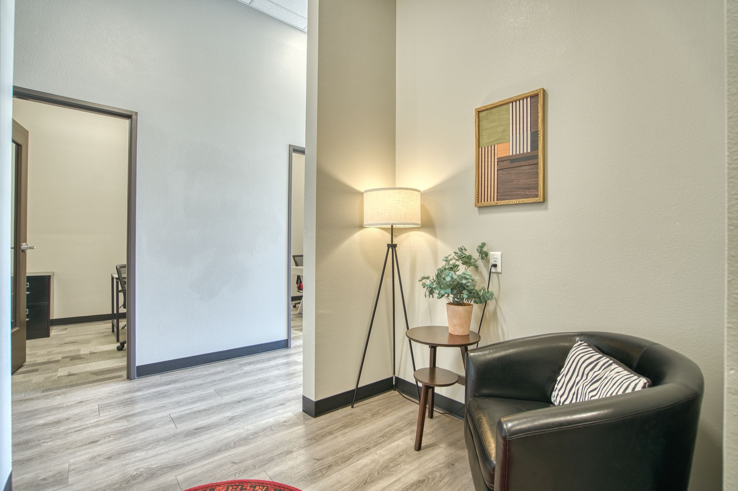 Cozy hallway reading nook with dark leather club chair, tripod floor lamp, and framed geometric artwork