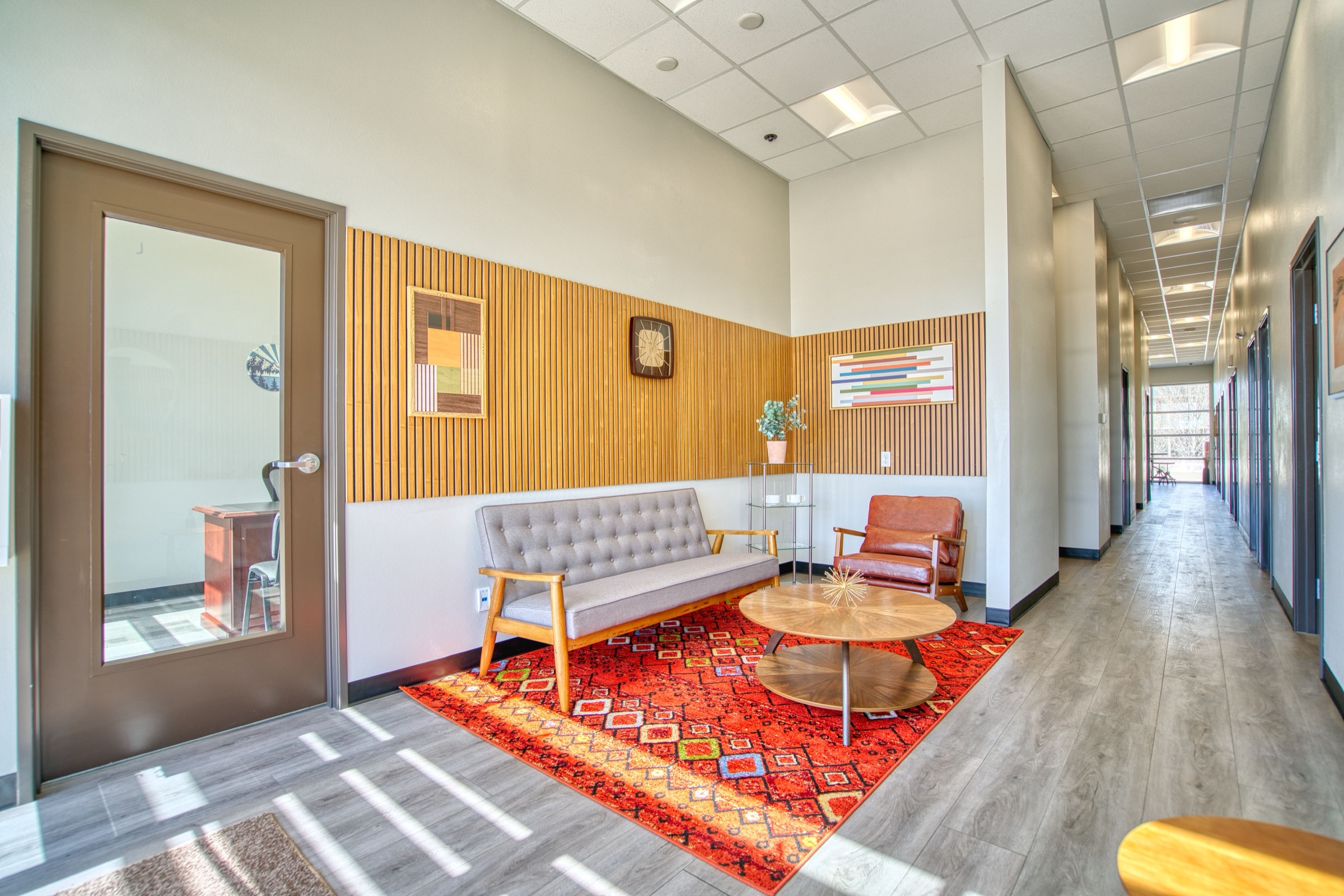 Leaf Coworking lobby lounge with tufted sofa, red geometric rug, and colorful wood slat accent wall with Colorado-inspired artwork
