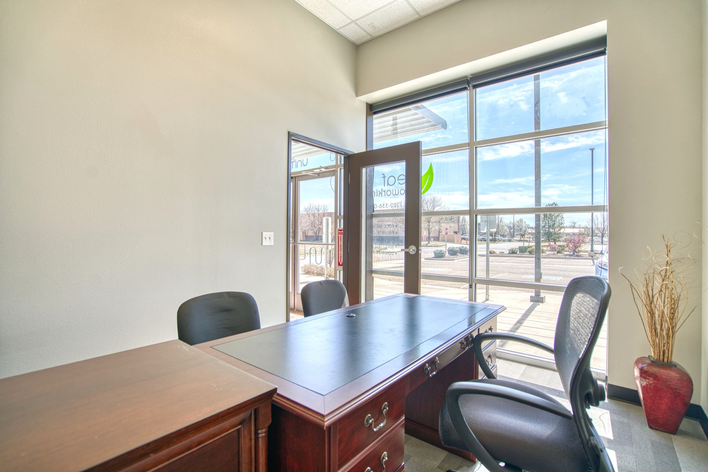 Private office at Leaf Coworking with executive desk facing floor-to-ceiling windows and natural light