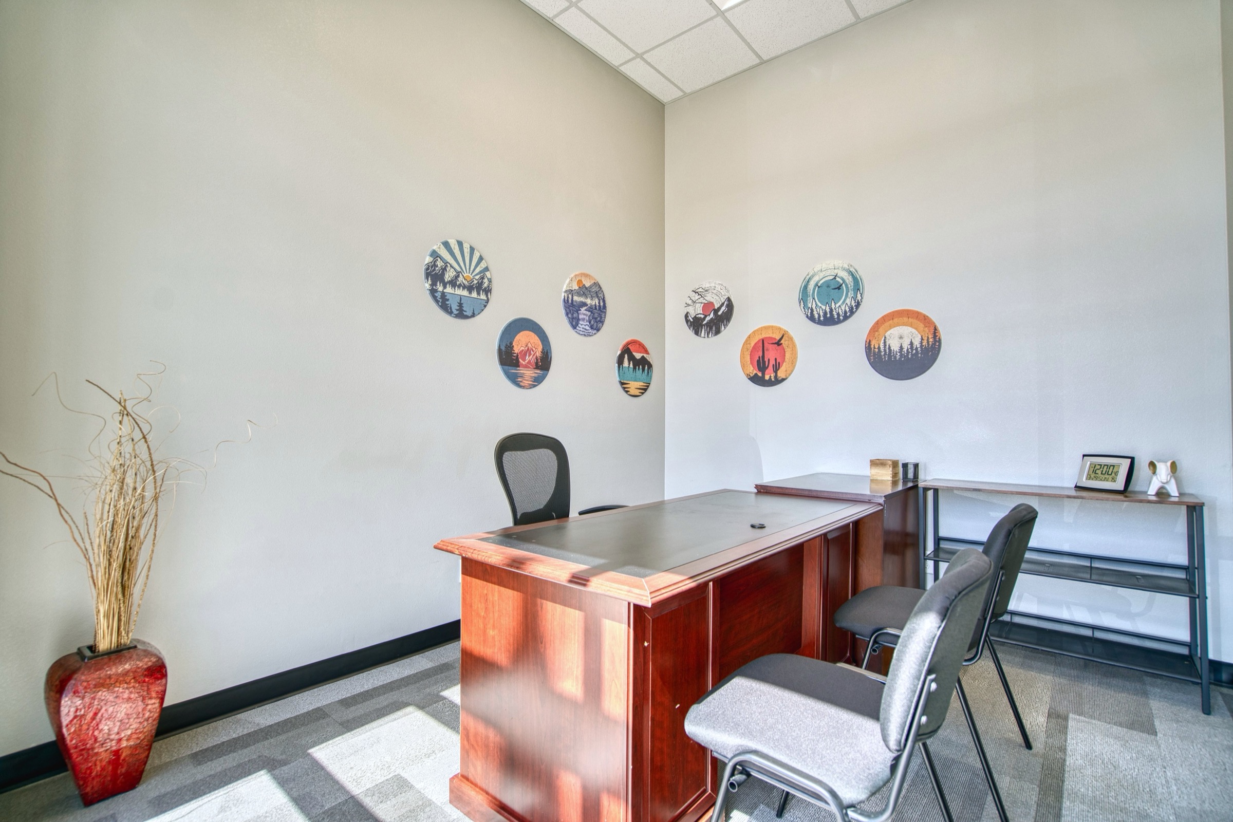 Furnished private office with cherry wood executive desk, ergonomic chair, guest seating, and circular Colorado landscape art